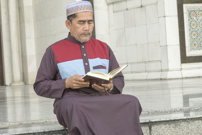 Young man reading book against built structure