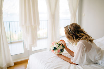 Rear view of woman sitting on bed at home