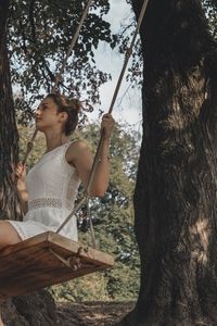 Woman sitting on swing amidst trees