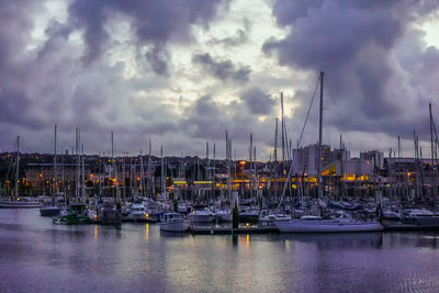 Sailboats moored on harbor against sky during sunset