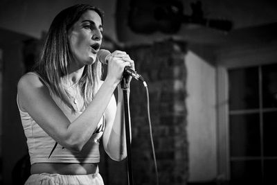 Young woman holding camera while standing against wall