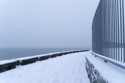 Snow covered railing by sea against clear sky