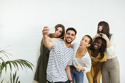 Playful colleagues standing at brick wall taking a selfie