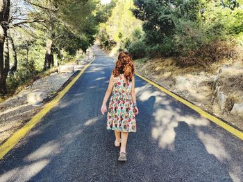 Rear view of woman walking on road amidst trees