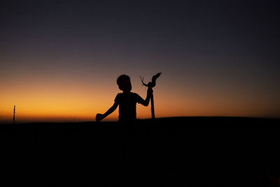 Silhouette of young child standing  against sky during sunset