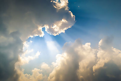 Low angle view of sunlight streaming through clouds