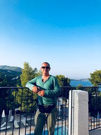 Full length of man standing by railing against clear blue sky