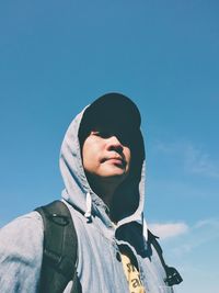 Portrait of man in hoodie against blue sky