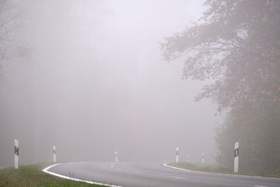 Road by trees against sky in foggy weather