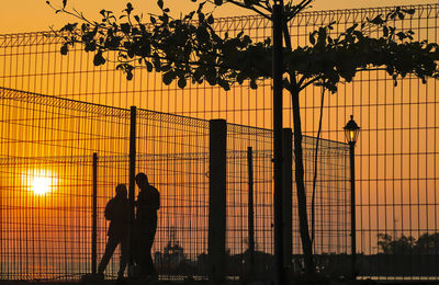 Silhouette people standing by tree against orange sky