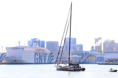 Sailboats in sea by buildings against clear sky