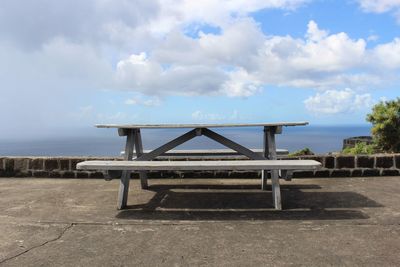 Empty benches on beach against sky