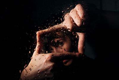 Young woman looking through window in dark room