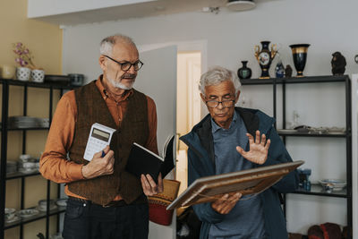 Senior male customer buying picture frame from salesman at antique shop