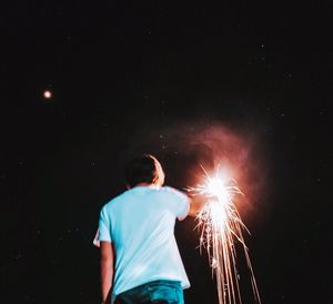 Rear view of man with arms outstretched at night