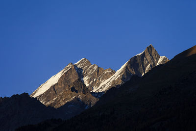 Low angle view of snowcapped mountains against clear blue sky