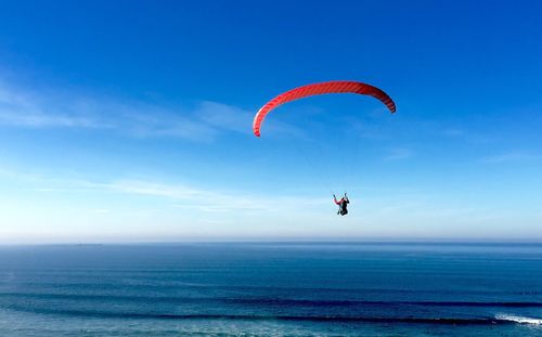 Person paragliding over sea against blue sky