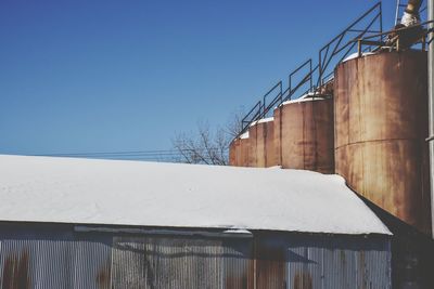 Snow covered barn by silos against clear sky