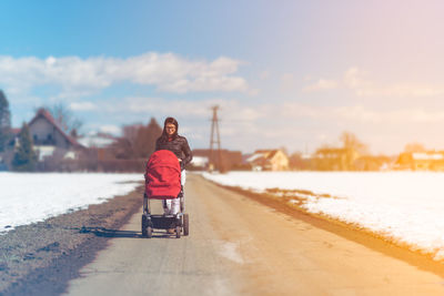 Woman with stroller walking on road against sky