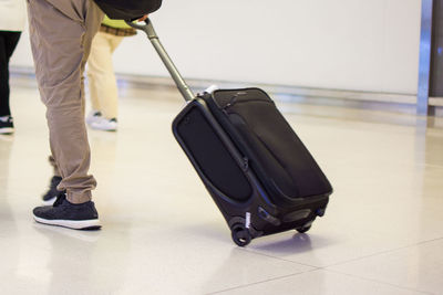 Low section of man with wheeled luggage on tiled floor at airport