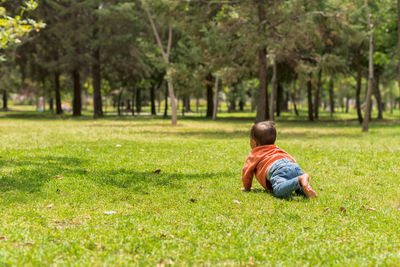 Full body of faceless barefoot little boy crawling on grassy lawn in sunny day in park