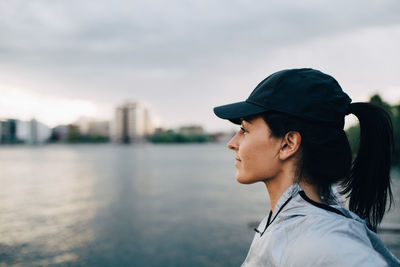 Side view of female athlete looking away while standing by sea against sky