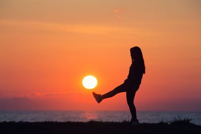 Silhouette woman standing against orange sky