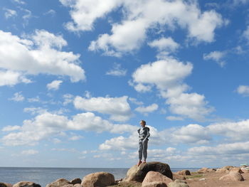 Girl standing on rock by sea against sky