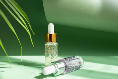 A variety of transparent cosmetic bottles with a pipette next to a palm leaf in the rays 