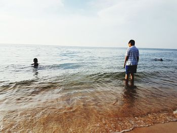 Rear view of boy standing on beach against sky