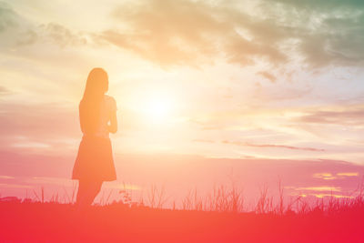 Woman standing on field against sky during sunset