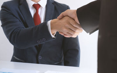 Midsection of businessman shaking hands with colleague over table in office