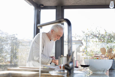 Senior man cooking while standing in kitchen at home