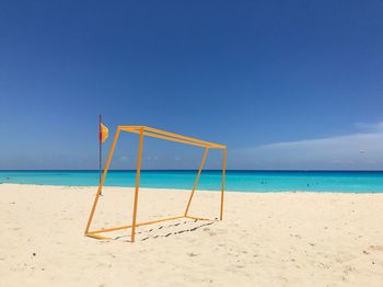 Soccer goal post at sandy beach against blue sky