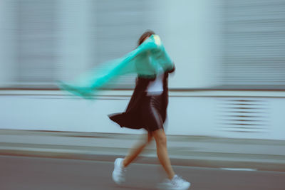 Side view of woman holding illuminated lighting equipment with scarf running on road in city
