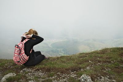 Full length of man sitting on mobile phone against sky