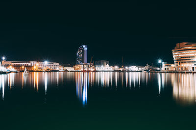 Illuminated city by sea against clear sky at night