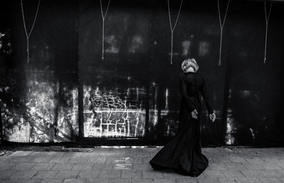 Rear view of woman standing by wall at night