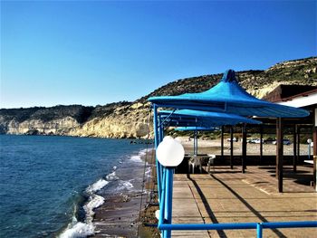 Deck chairs by sea against clear blue sky