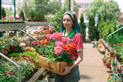 Portrait of gardener holding flowers in container at greenhouse