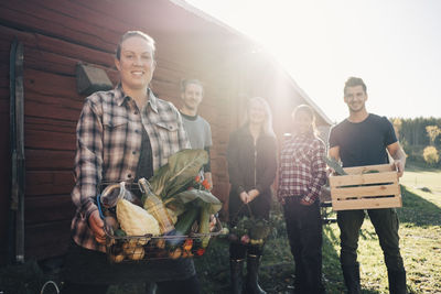 Portrait of smiling farmers carrying organic vegetables outside barn