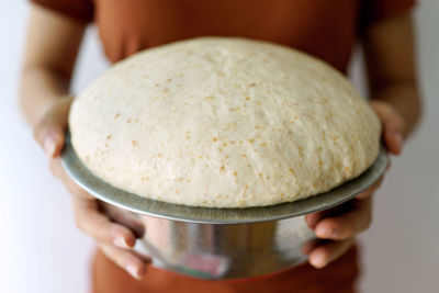 Midsection of woman holding bread dough in container at home