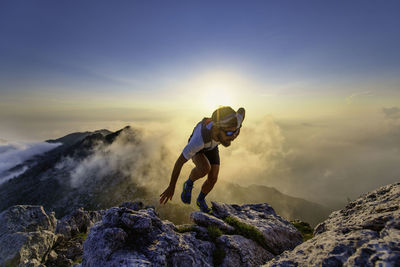 Rear view of woman walking on mountain against sky during sunset