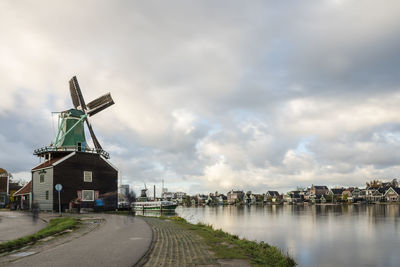 Traditional windmill by river against sky