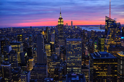 Illuminated cityscape against romantic sky at sunset