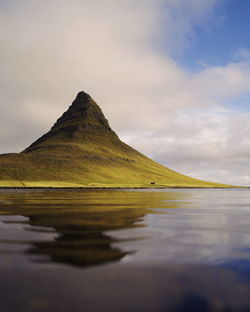 Scenic view of sea by mountain against sky