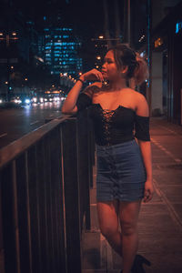 Full length of woman standing by illuminated city at night