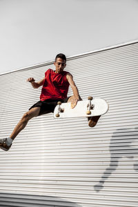 Man with skateboard in mid-air against wall