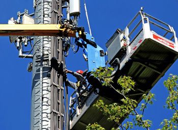 Low angle view of electrician working on pylon against sky