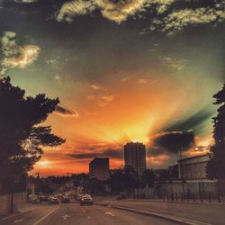 Cars on road against dramatic sky during sunset